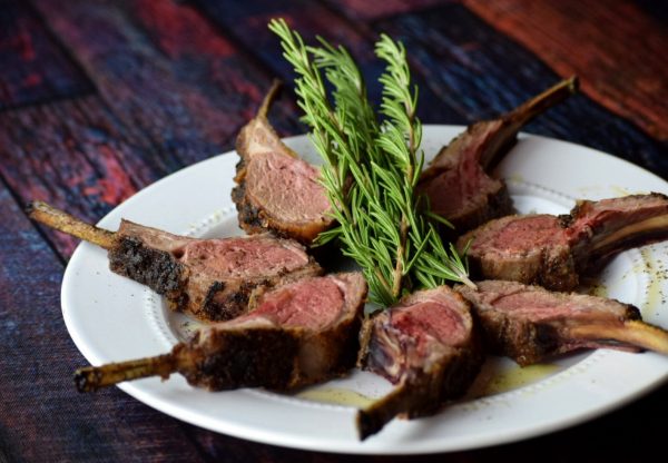Honey and herb crusted rack of lamb carved and places on a white plate with rosemary.