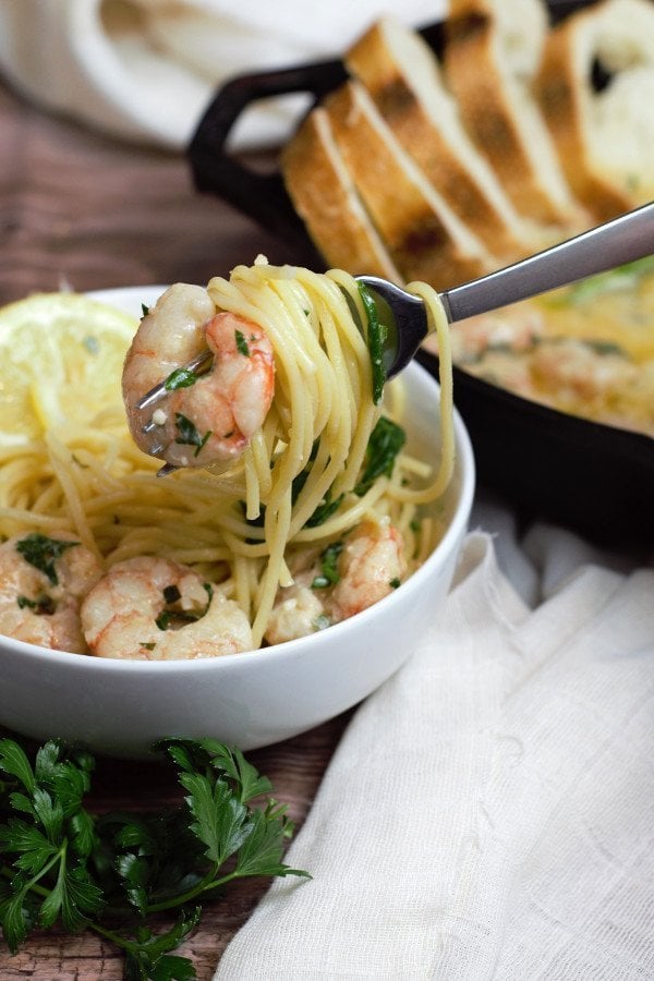 Noodles with butter twirled around a fork with a piece of shrimp scampi on the end.