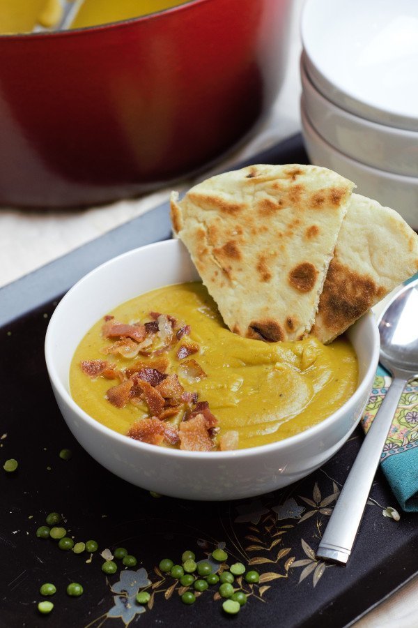 white bowl of split pea soup with naan bread and a red pot behind it.