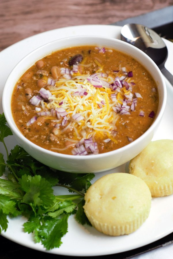 Chili in a white bowl with corn bread and cilantro