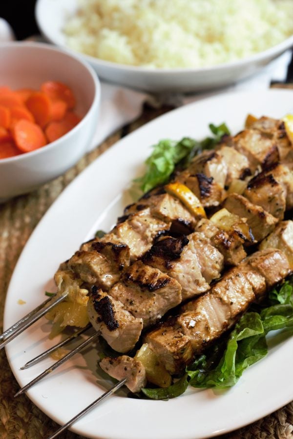grilled pork souvlaki skewers alongside glazed carrots and rice pilaf.