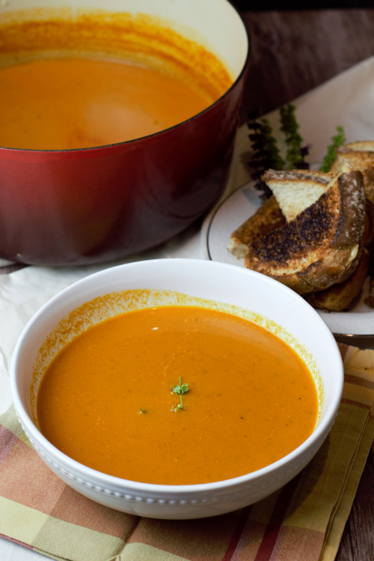 Bowl of tomato bisque with side of grilled cheese in front of soup pot
