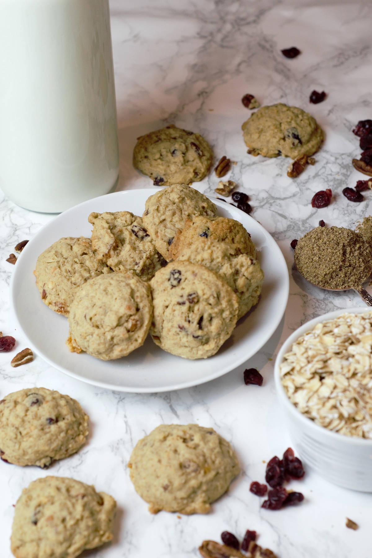 Plate of breakfast cookies with pitcher or milk, bowl of oats, and spoon of flax