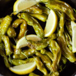 blistered shishito peppers in cast iron pan with lemon wedges