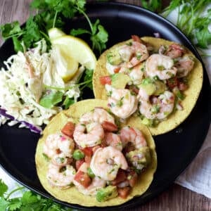 two shrimp tostadas with toppings on side of black plate