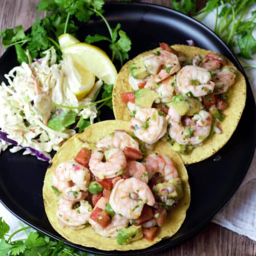 two shrimp tostadas with toppings on side of black plate