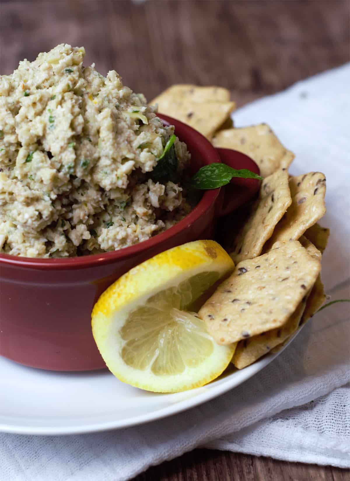 pesto in red bowl surrounded by crackers