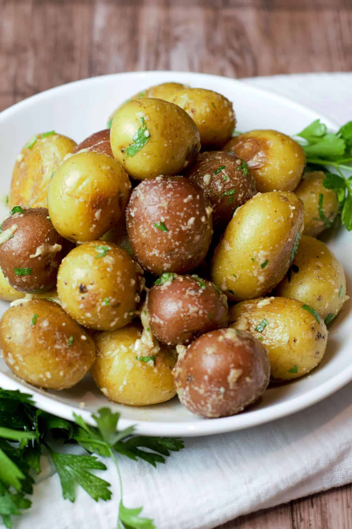 close up of new potatoes with parmesan, garlic, and parsley in a white bowl