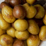 overhead of browned new potatoes with sage leaves in a white bowl
