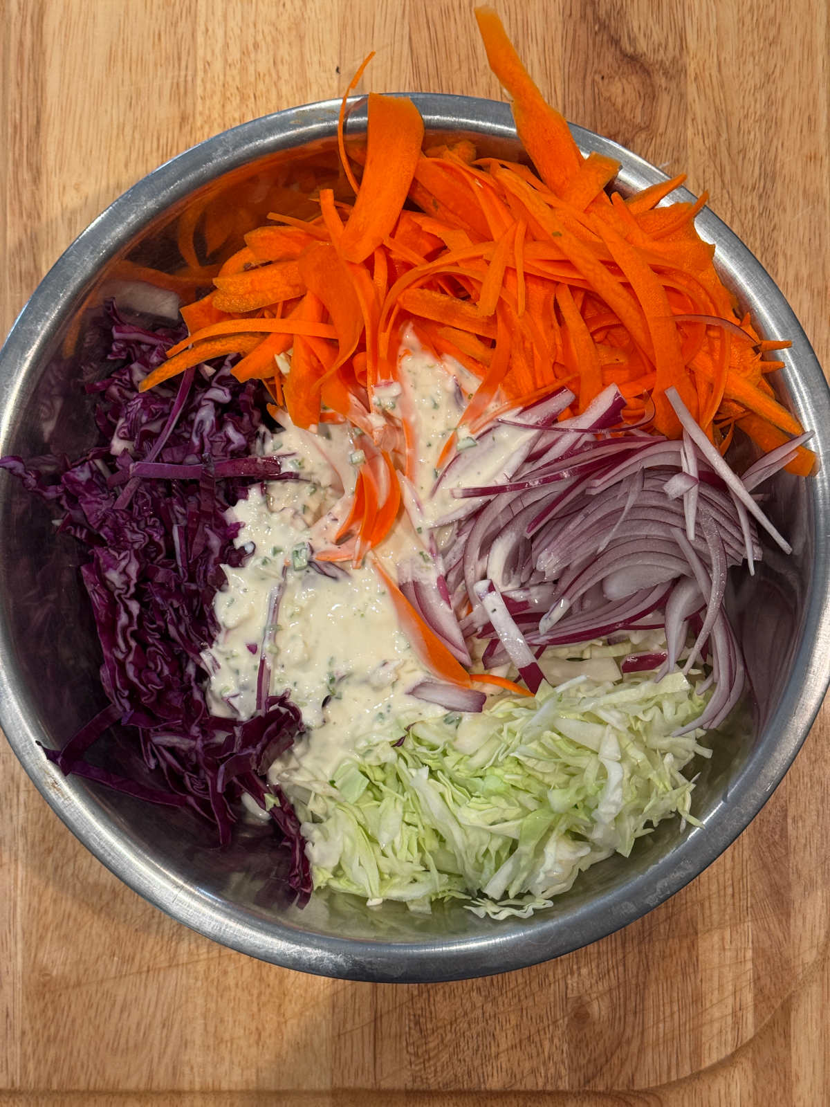 sliced cabbage, carrots, onions with dressing in the middle of a metal bowl