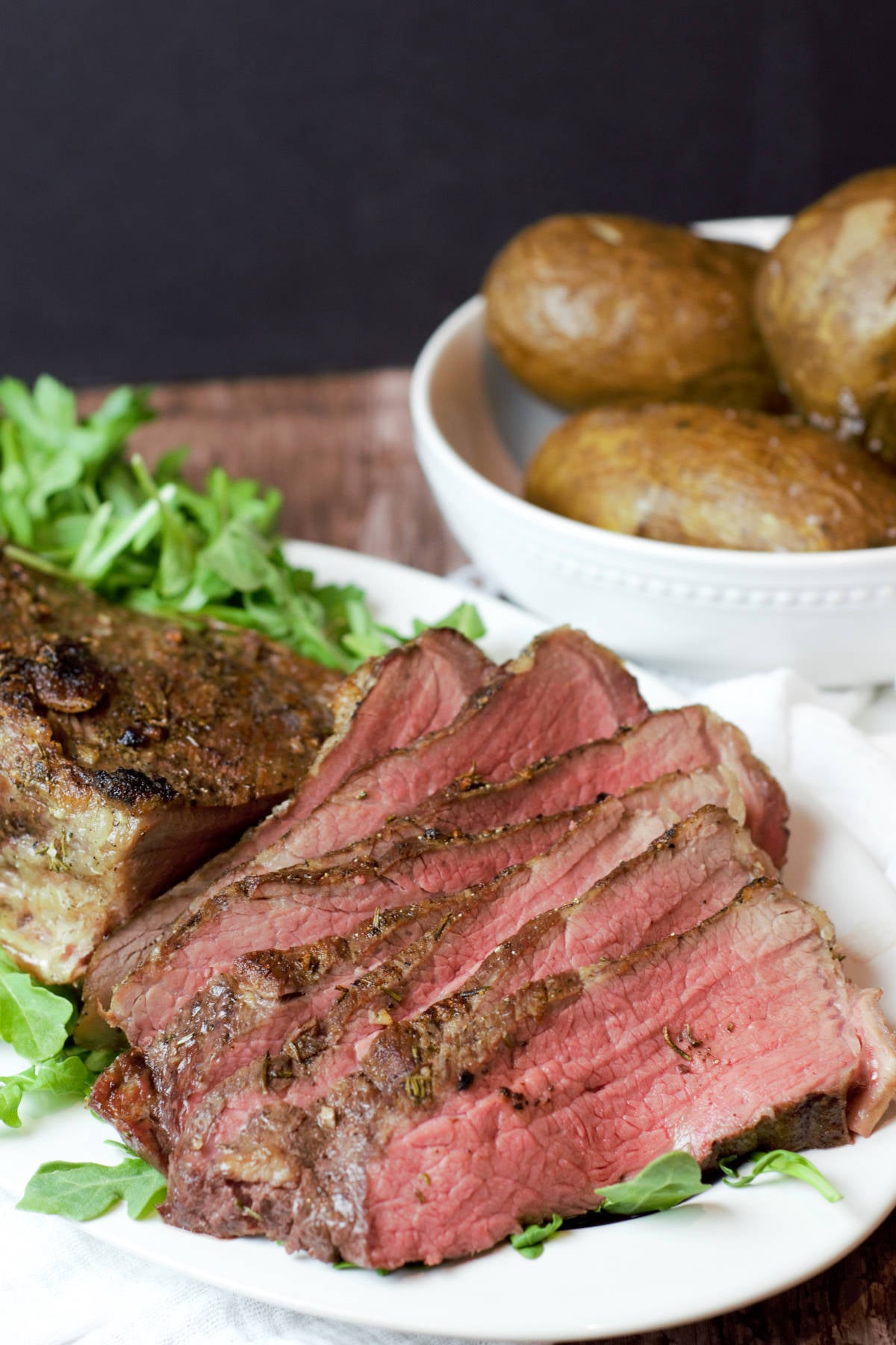 close up tri tip on greens with potatoes in background